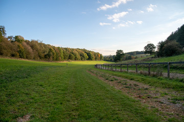 Autumn fields in English countryside with fenced track, blue skies and white clouds