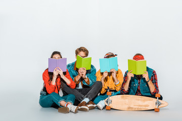 young students sitting with skateboard and holding books together