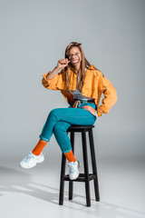 stylish smiling girl holding magnifier while sitting on stool on grey