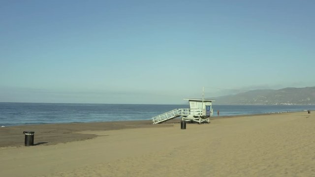 Steadicam shot flying towards a lifeguard hut on the beach during the day.