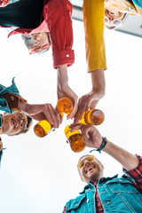 bottom view of young friends clinking with beer bottles together