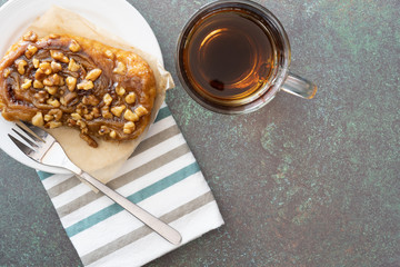 dessert of sticky bun on a white plate with fork and striped napkin and coffee on green background