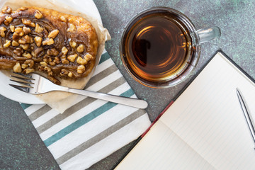 break time with a sticky bun on a white plate with fork and striped napkin and a cup of coffee and lined paper notebook and pen