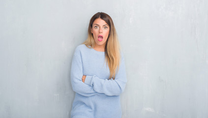 Young adult woman over grey grunge wall wearing winter outfit afraid and shocked with surprise expression, fear and excited face.