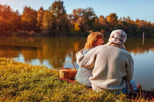 Senior couple having picnic by autumn lake. Happy man and woman enjoying nature and hugging - Powered by Adobe