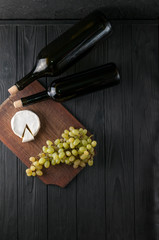 Bottles of wine on a black wooden background with grapes and cheese Camemberg