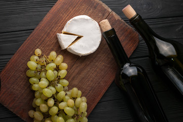 Bottles of wine on a black wooden background with grapes and cheese Camemberg