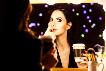 portrait of young beautiful woman with cup of coffee looking in the mirror
