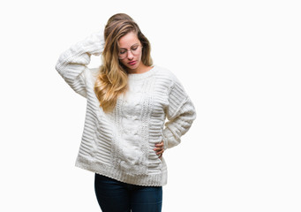 Young beautiful blonde woman wearing winter sweater and sunglasses over isolated background confuse and wonder about question. Uncertain with doubt, thinking with hand on head. Pensive concept.