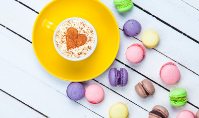 Cup of Cappuccino with heart shape symbol and macaron on white wooden background