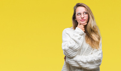 Young beautiful blonde woman wearing winter sweater and sunglasses over isolated background looking confident at the camera with smile with crossed arms and hand raised on chin. Thinking positive.