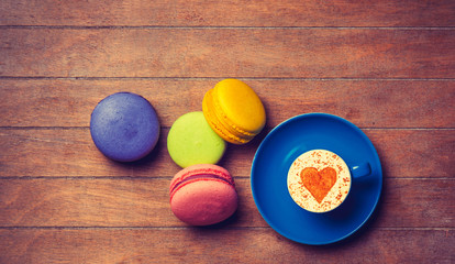Cup of Cappuccino with heart shape symbol and macarons on wooden background
