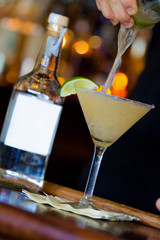 Martini drink and limes on bar with blank bottle, bartender, and bokeh 2