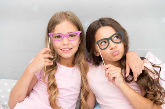 Girls children posing with grimaces photo booth props. Pajamas party concept. Girls friends having fun pajamas party. Friends cheerful posing with eyeglasses accessories for party. Playful mood