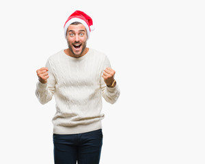 Naklejka premium Young handsome man wearing santa claus hat over isolated background celebrating surprised and amazed for success with arms raised and open eyes. Winner concept.