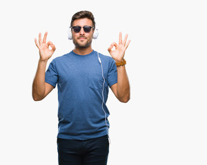 Naklejka premium Young handsome man wearing headphones listening to music over isolated background relax and smiling with eyes closed doing meditation gesture with fingers. Yoga concept.