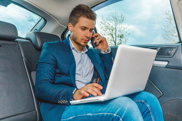 бизнесмен сидит на заднем сиденье авто с ноутбуком, разговаривает по телефону