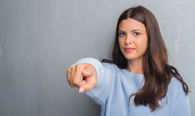 Young brunette woman over grunge grey wall pointing with finger to the camera and to you, hand...