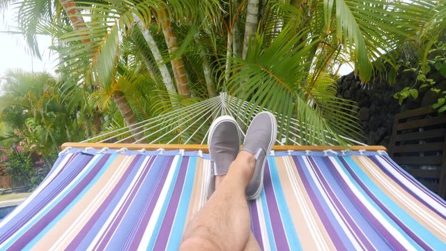 Hammock Swing Point of View Tlit Down. a slow motion personal point of view of a male swinging on a hammock, tilt down from palm trees to legs on hammock