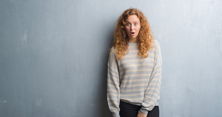 Naklejka premium Young redhead woman over grey grunge wall afraid and shocked with surprise expression, fear and excited face.