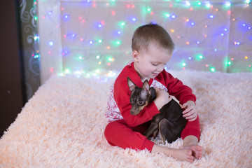 little boy in red pajamas playing with a dog on Christmas Eve