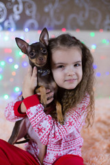 Beautiful little girl in New Year's pajamas. A child hugs a toy terrier dog