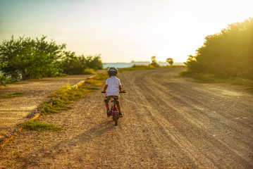 Boy drives bicycle towards sunset on the horizon the unfocused sea and natural sunlight from the side                 