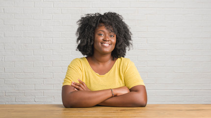 Young african american woman sitting on the table at home happy face smiling with crossed arms looking at the camera. Positive person.