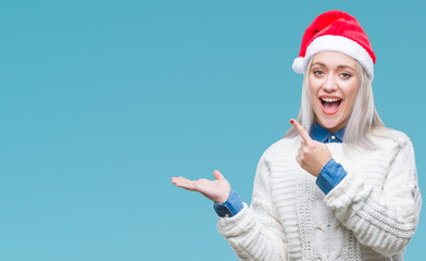 Fototapeta na wymiar Young blonde woman wearing christmas hat over isolated background amazed and smiling to the camera while presenting with hand and pointing with finger.