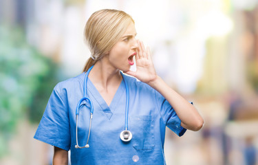 Young beautiful blonde doctor surgeon nurse woman over isolated background shouting and screaming loud to side with hand on mouth. Communication concept.