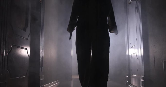 Creepy silhouette in the dark abandoned building. Horror Halloween concept. Dark corridor with silhouette of horror person standing in center. Toned light and fog on background.