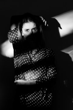 Portrait of a woman with shadows on face, wearing a polka dot blouse. Converted to black and white, grain added.