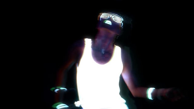 Beautiful sexy woman with UV face paint, glowing clothing, glowing glasses, bracelet dancing in front of camera, half body shot. Asian woman. Glitch effect. Party concept.