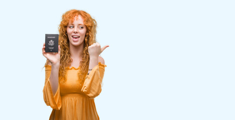 Young redhead woman holding passport of United States of America pointing and showing with thumb up to the side with happy face smiling
