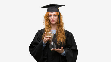 Young redhead student woman wearing graduated uniform holding hourglass with a confident expression on smart face thinking serious