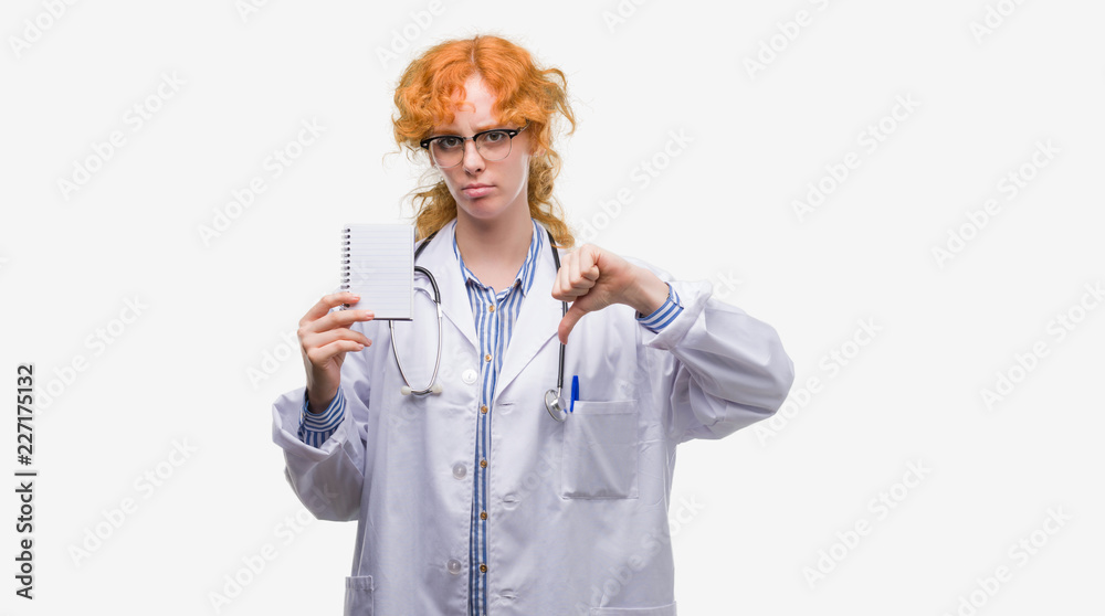 Sticker young redhead doctor woman holding blank notebook with angry face, negative sign showing dislike wit