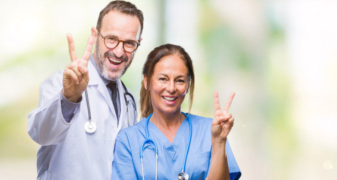 Middle age hispanic doctors partners couple wearing medical uniform over isolated background smiling with happy face winking at the camera doing victory sign. Number two.