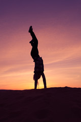 Silhouette of woman doing hand stand on sand dune during the sunset