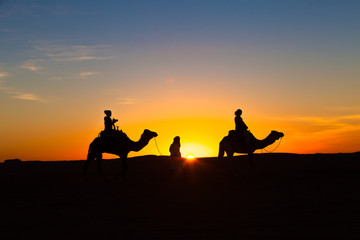 Fototapeta na wymiar Silhouette of two people on camels on a dune during the sunset