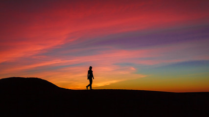 Silhouette of woman walking on sand dune during the sunset