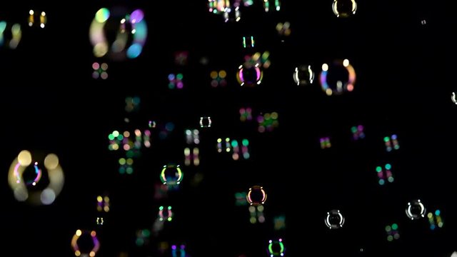 Soap bubbles fly in the air and shimmer in different colors. Black background