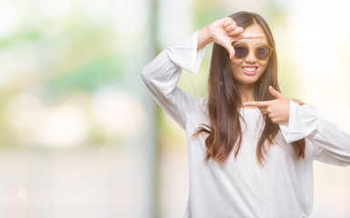 Young asian woman wearing sunglasses over isolated background smiling making frame with hands and fingers with happy face. Creativity and photography concept.