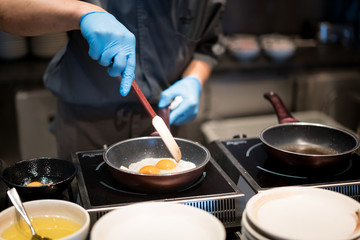 Hotelchef-kok handen met handschoenen koken gebakken eieren op hete pan voor ontbijt in restaurant in hotel.