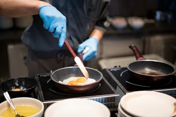 Muurstickers Koken Hotelchef-kok handen met handschoenen koken gebakken eieren op hete pan voor ontbijt in restaurant in hotel.