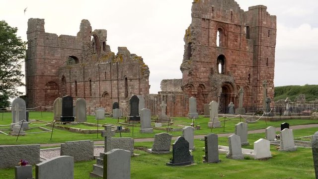 Zoom in-Church cemetery head stones to the historic ruins on the Lindisfarne Priory on tidal Holy Island off the northeast coast of England