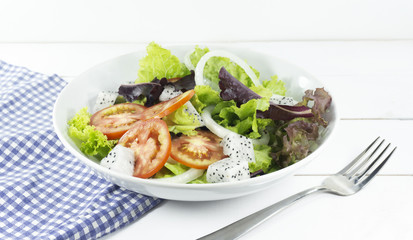 Healthy salad diet food concept, props decoration fork and blue Napery, tomatoes Dragon fruit and green and Purple Salad in white Plate on wood floor background, Close up, with copy space.