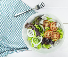 Fresh Green salad Healthy diet food concept, props decoration fork and blue Napery, tomatoes Dragon fruit and green and Purple Salad measuring tape in white Plate on wood floor background, Top up.