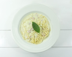 Spaghetti Carbonara in a dish White leaves green basil placed on top Bacon and milk line yellow on white wood floor table,Top view,Copy space Close up..
