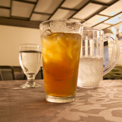 glass of cold iced tea with ice and goblet and pitcher of water on restaurant table