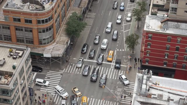 A high angle view of a typical midtown Manhattan intersection as traffic and pedestrians travel on the streets below.  	